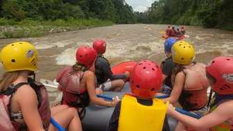 Eine Gruppe von Menschen im Kanu trägt bunte Helme und Schwimmwesten, während sie einen reißenden Fluss befahren.