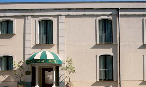 Das Katane Palace Hotel zeigt eine elegante Fassade mit einem markanten grünen und weißen Vordach und großen Fenstern.