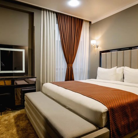 Ein modernes Hotelzimmer mit einem großen Bett, eleganten Vorhängen und einem stilvollen Schminktisch im Hintergrund.