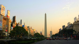 Der Obelisk von Buenos Aires erhebt sich majestätisch über eine belebte Straße, umgeben von modernen Gebäuden und Werbetafeln.