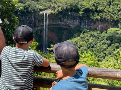 Zwei Kinder stehen an einem Geländer und blicken auf den beeindruckenden Chamarel-Wasserfall in Mauritius.
