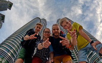 Familie posiert fröhlich für ein Selfie mit den Petronas Twin Towers im Hintergrund – Malaysia & Borneo Reise mit Kindern