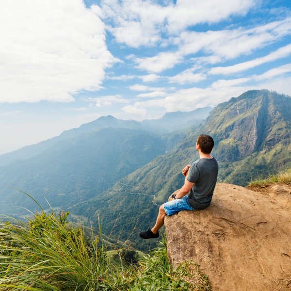 Teenager sitzt auf einem Felsen und blickt auf die grüne Berglandschaft bei Ella – Sri Lanka Familienreise