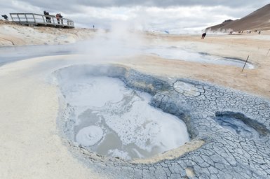 Dampfsäulen steigen aus heißen Quellen auf, während Besucher auf einer Aussichtsplattform die geothermische Landschaft bewundern.