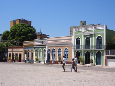 Drei Personen spazieren entspannt auf einem Pflasterweg, umgeben von bunten historischen Gebäuden in Manaus.