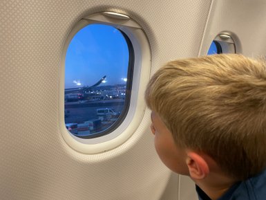 Ein Junge blickt neugierig aus dem Fenster eines Flugzeugs beim Landeanflug – Südafrika Reise mit Kindern