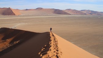 Eine Mutter steht mit ihrem Kind auf dem Arm auf einer Düne - Namibia Reise mit Kindern