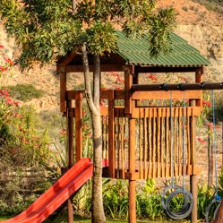 Ein Spielplatz mit einer Rutsche und Schaukeln, umgeben von bunten Blumen und einem malerischen Hügel im Hintergrund.