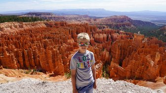 Ein Junge mit Sonnenbrille steht vor den beeindruckenden, orangefarbenen Felsformationen des Bryce Canyon Nationalparks.