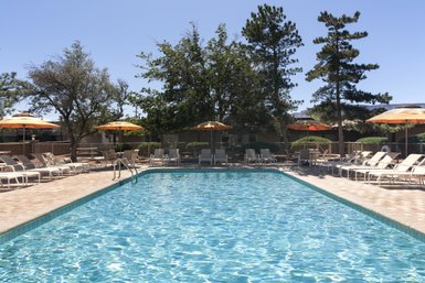 Ein einladender Pool mit klarem Wasser, umgeben von Liegen und Sonnenschirmen, unter einem strahlend blauen Himmel.