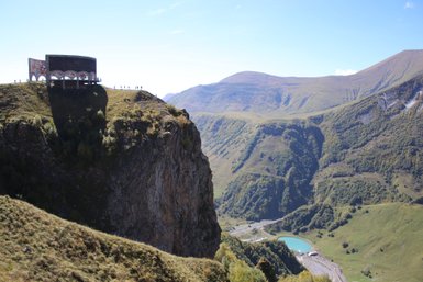 Ein beeindruckender Blick auf die Berge des Kaukasus, mit einer markanten Struktur auf einer Klippe im Vordergrund.