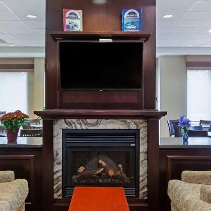 Ein einladender Aufenthaltsraum mit bequemen Sofas, einem Kamin und einem Fernseher über dem Kamin, ideal zum Entspannen.