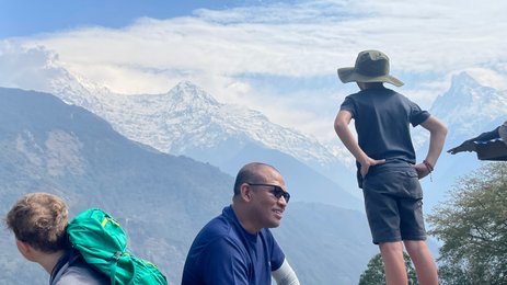 Ein Junge mit einem Hut steht nachdenklich auf einem Felsen und blickt auf die majestätischen schneebedeckten Berge.