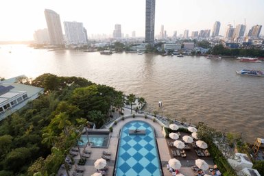 Ein Blick auf den Pool des Chatrium Hotels, umgeben von Palmen und Liegen, mit der Stadt Bangkok im Hintergrund.