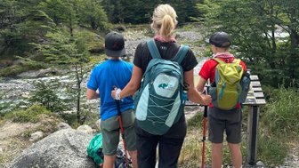 Eine Frau steht mit zwei Kindern am Wanderweg und blickt auf die beeindruckenden Berge im Hintergrund.