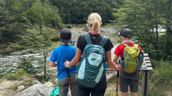 Eine Frau steht mit zwei Kindern am Wanderweg und blickt auf die beeindruckenden Berge im Hintergrund.