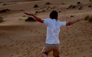 Ein Junge springt fröhlich über die Sanddünen, während die Sonne am Horizont untergeht und den Himmel in warmen Farben färbt.