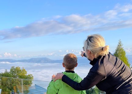 Eine Frau zeigt einem Jungen die majestätischen Himalaya-Berge, während sie über eine Wolkendecke blicken.