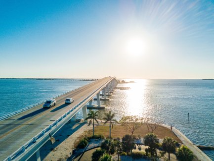 Eine malerische Brücke erstreckt sich über das glitzernde Wasser, während Autos in der warmen Sonne fahren.