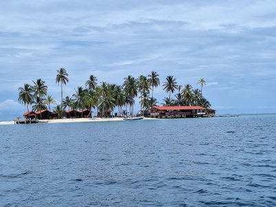 Eine malerische Insel mit Palmen und roten Dächern, die am Ufer eines ruhigen, blauen Meeres liegt.