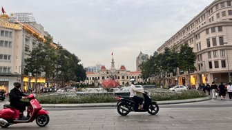 Eine belebte Straße in Saigon mit Motorrädern und einem großen Brunnen im Vordergrund, umgeben von historischen Gebäuden.