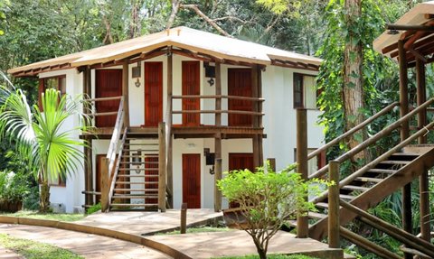 Ein modernes zweigeschossiges Haus mit Holzverkleidung, umgeben von üppigem Grün und tropischen Pflanzen.