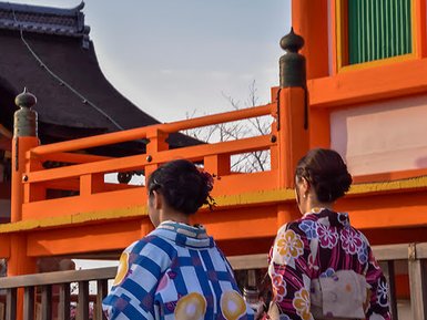 Zwei Frauen in bunten Kimonos stehen vor einem leuchtend orangefarbenen Tor in Kyoto und genießen die Aussicht.