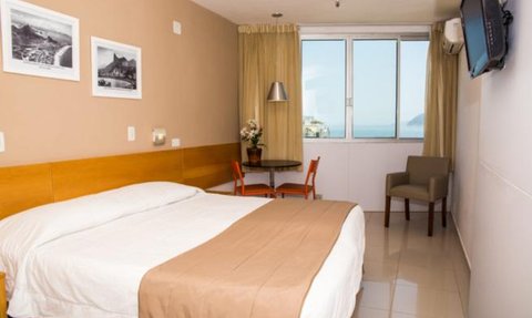 Ein helles Hotelzimmer mit einem großen Doppelbett, Holzmöbeln und Blick auf das Meer durch ein großes Fenster.