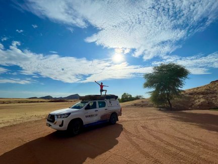 Ein Mädchen posiert für eine Foto in der Wüste auf dem Autodach - Namibia Urlaub mit Kindern