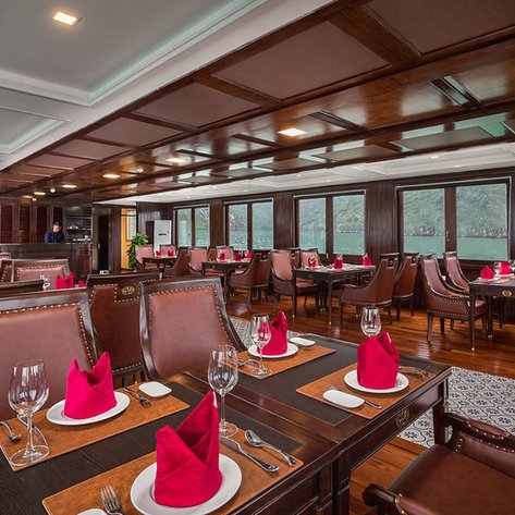 Elegante Restaurant mit Holzdekor, stilvollen Tischen und roten Servietten, umgeben von großen Fenstern mit Blick auf die Natur.