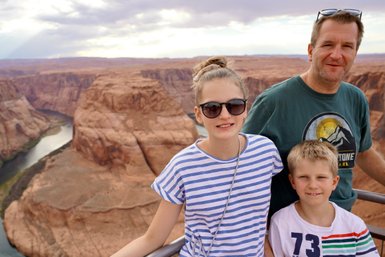 Eine Familie steht am Rand des Horseshoe Bend, umgeben von beeindruckenden roten Felsen und einem Fluss im Hintergrund.