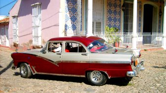 Ein klassischer Oldtimer in rot und silber parkt auf einem gepflasterten Weg vor einem bunten, historischen Gebäude.