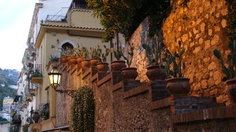 Eine malerische Gasse in Taormina, gesäumt von Töpfen mit Kakteen und warmem Licht, das die Steine beleuchtet.