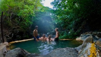 Gruppe von vier Personen in einem natürlichen Pool, umgeben von üppiger, grüner Vegetation in einem ruhigen Dschungelsetting.