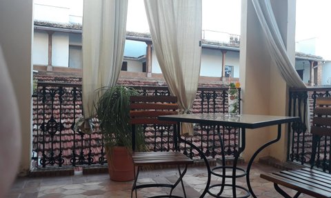 Ein gemütlicher Balkon mit einem Tisch und zwei Stühlen, umgeben von sanften Vorhängen und einer Pflanze im Topf.