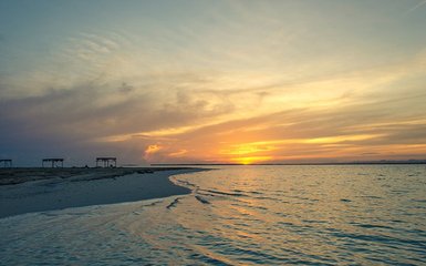 Ein atemberaubender Sonnenuntergang über dem ruhigen Wasser, das sanft an den Strand plätschert.