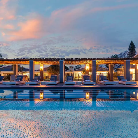 Ein eleganter Poolbereich mit Liegen, umgeben von sanften Lichtern und einem malerischen Abendhimmel.