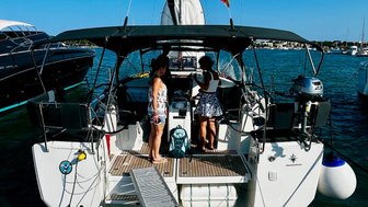 Zwei Frauen stehen auf einem Segelboot, das an einem Steg im Hafen festgemacht ist, umgeben von anderen Yachten.