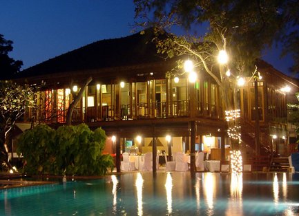 Ein elegantes Restaurant mit Holzverkleidung, das über einem glitzernden Pool thront, umgeben von sanfter Beleuchtung.