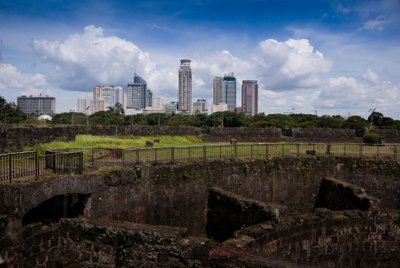 Die Ruinen von Fort Santiago sind im Vordergrund zu sehen, während moderne Wolkenkratzer die Skyline von Manila bilden.