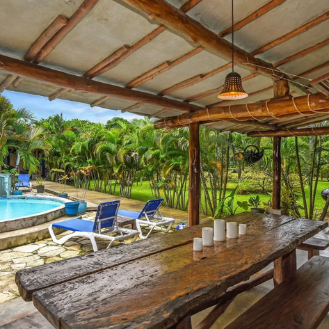 Ein einladender Außenbereich mit einem Pool, umgeben von üppigem Grün und einem rustikalen Holztisch im Vordergrund.