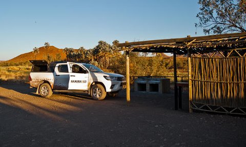 Ein weißes Fahrzeug steht an einem abgelegenen Campingplatz in Namibia, umgeben von sanften Hügeln und Bäumen.