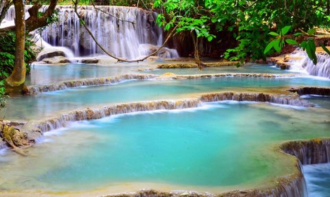Die Kuang Si Wasserfälle zeigen mehrere kaskadierende Wasserfälle, die in türkisfarbenen Becken landen, umgeben von üppigem Grün.