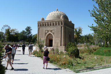 Eine Gruppe von Touristen erkundet das Samaniden-Mausoleum, umgeben von üppigem Grün und bunten Blumen im Park.