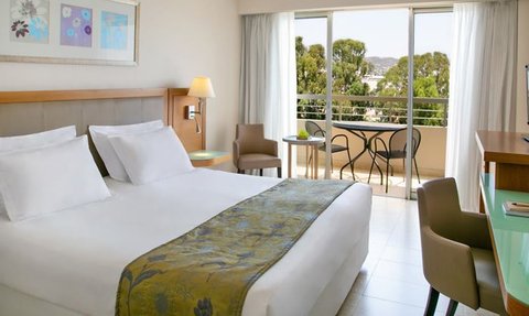 Ein helles Hotelzimmer mit einem großen Bett, das mit einer grünen Decke dekoriert ist, und einem Balkon mit Blick auf die Natur.