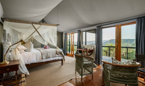 Ein elegantes Schlafzimmer mit einem Himmelbett, umgeben von großen Fenstern, die einen atemberaubenden Ausblick bieten.