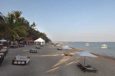 Ein ruhiger Strand in Bali mit Liegen, Sonnenschirmen und Palmen, ideal für einen entspannten Familienurlaub.