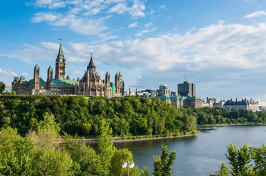 Die beeindruckende Parlamentsgebäude von Ottawa erhebt sich majestätisch über den grünen Hügel, umgeben von strahlend blauem Himmel.
