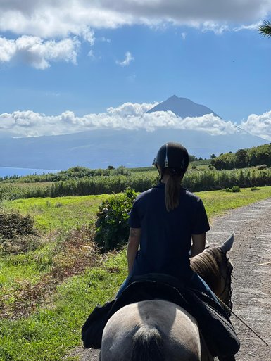 Eine Person sitzt auf einem Pferd und blickt auf eine grüne Landschaft mit einem majestätischen Berg im Hintergrund.