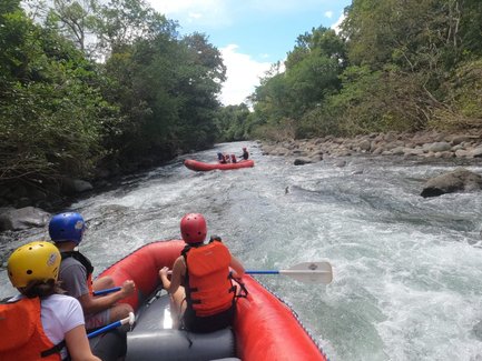 Eine Gruppe von Menschen paddelt in einem roten Schlauchboot auf einem reißenden Fluss, umgeben von üppigem Grün.